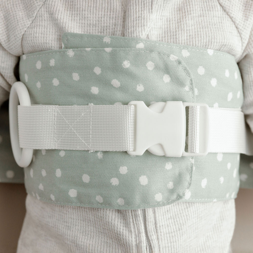 Close up of the sage green WriggleBum nappy change harness, with white straps and a white buckle