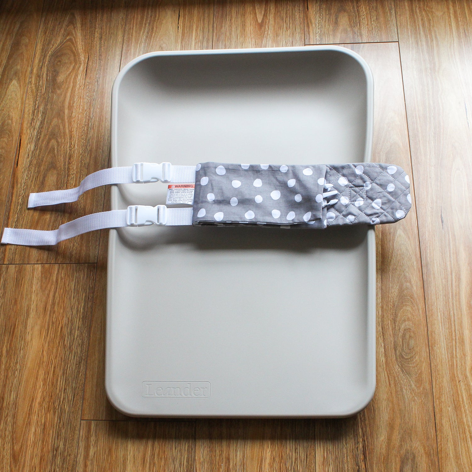 A grey and white WriggleBum nappy change harness is wrapped around a change mat and the two straps are fastened.