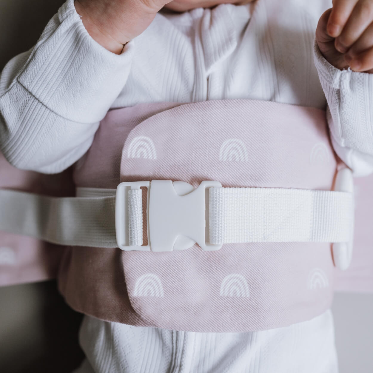 A close up of the Rainbow Blush WriggleBum nappy change harness, wrapped around a baby.