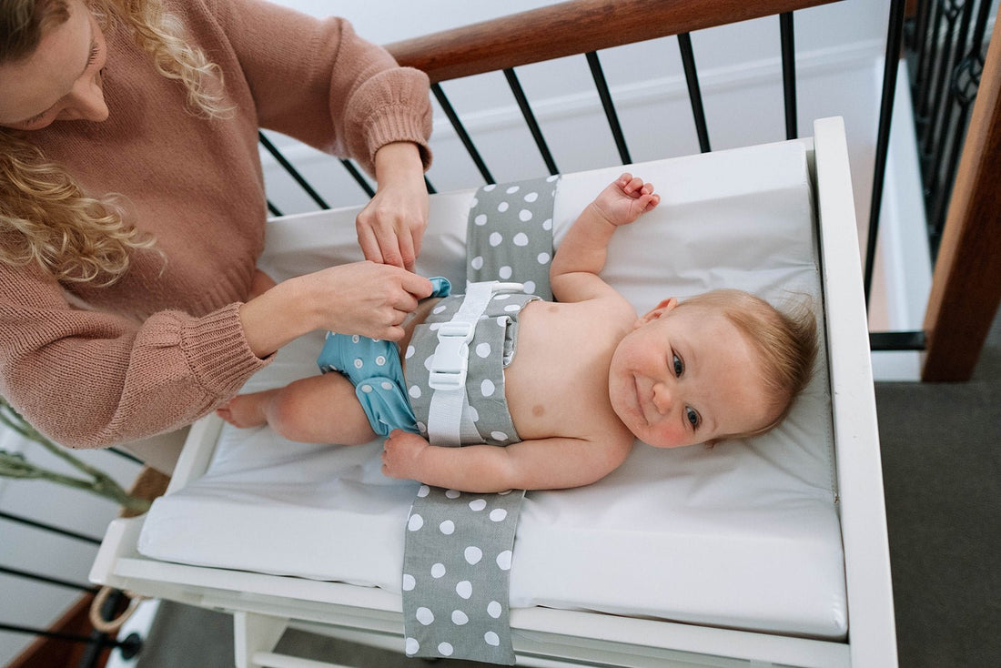 Baby in lying on a change table, wrapped in a WriggleBum nappy change harness, while his mum adjusts his cloth nappy.