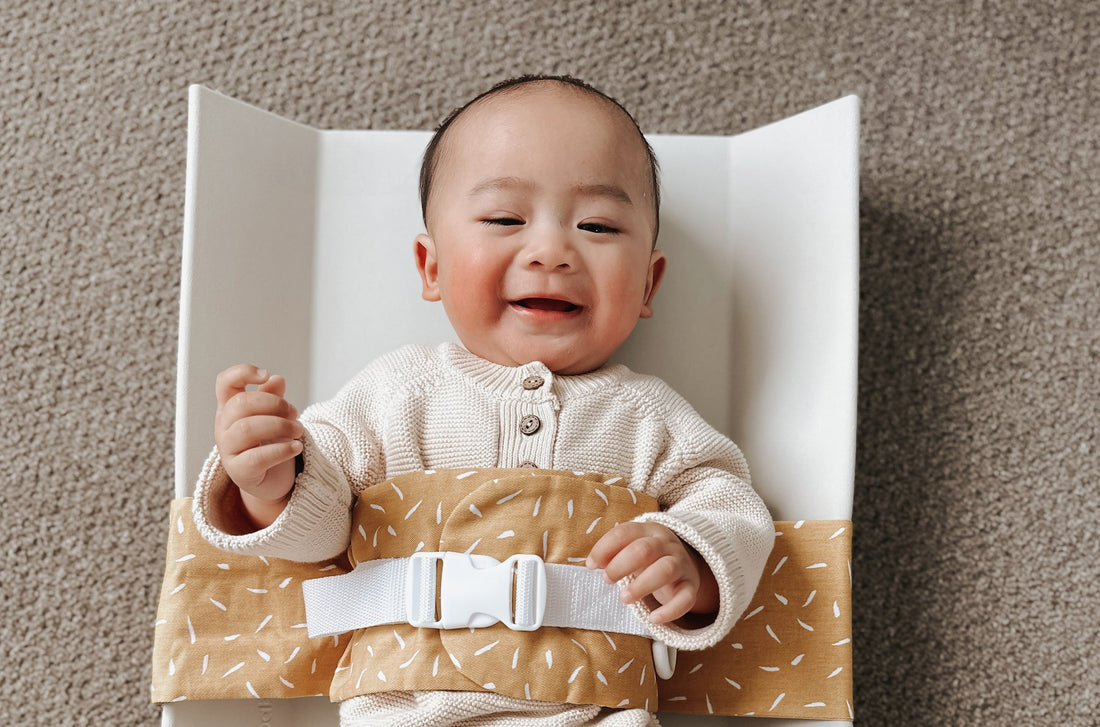 Smiling baby on a solid change mat is wrapped in a Butterscotch Sprinkle WriggleBum nappy change harness.