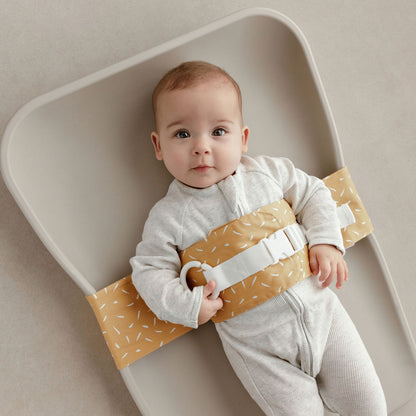 Wriggly baby in mustard Butterscotch Sprinkle WriggleBum nappy change harness, lying on a Leander Matty change mat