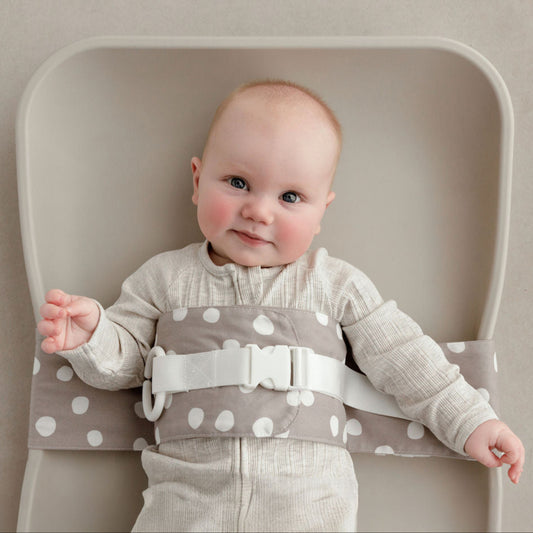 Wriggly smiling baby in grey and white Spotty Dotty WriggleBum nappy change harness, lying on a Leander Matty change mat 