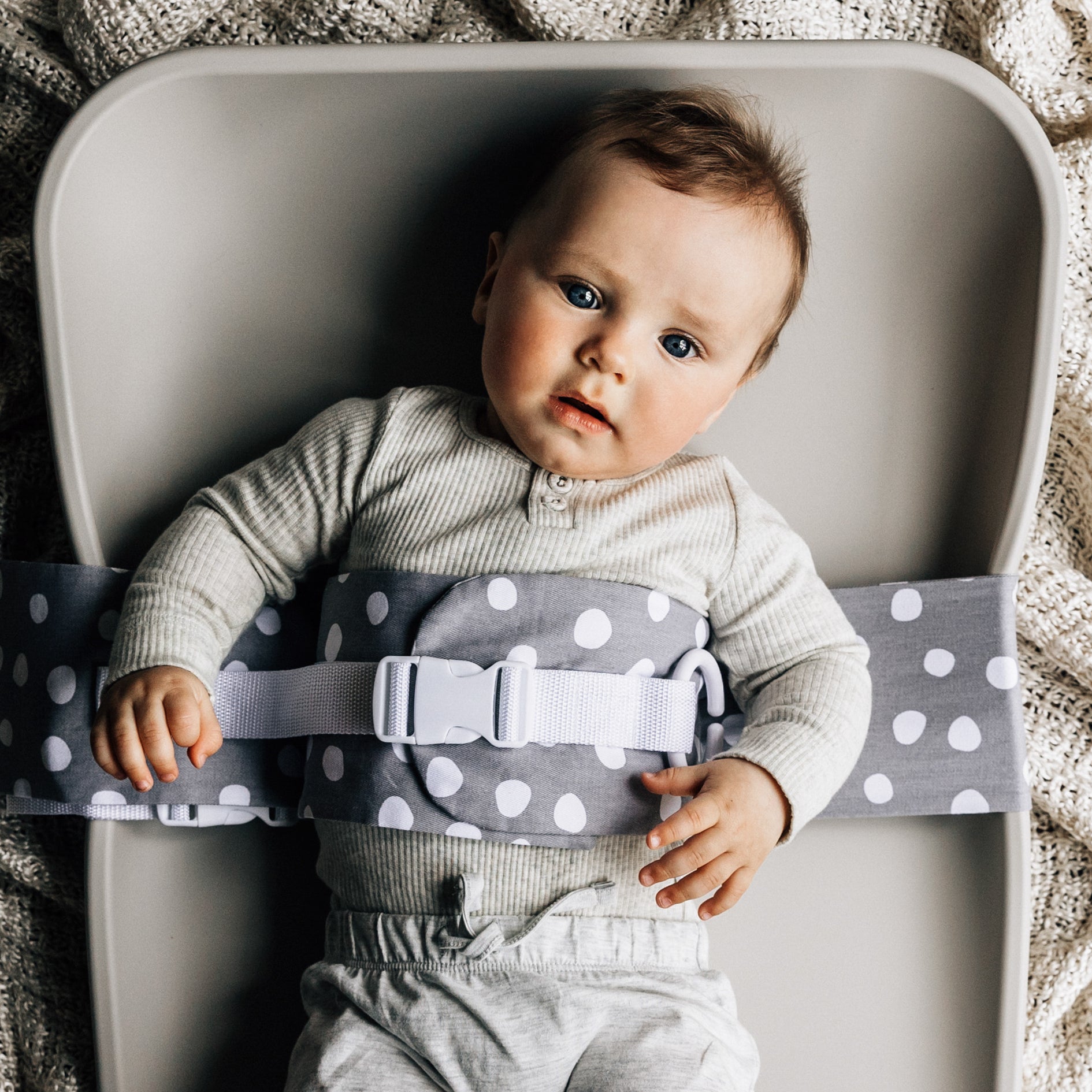 A grey WriggleBum nappy change harness is fasted around a baby on a change mat.