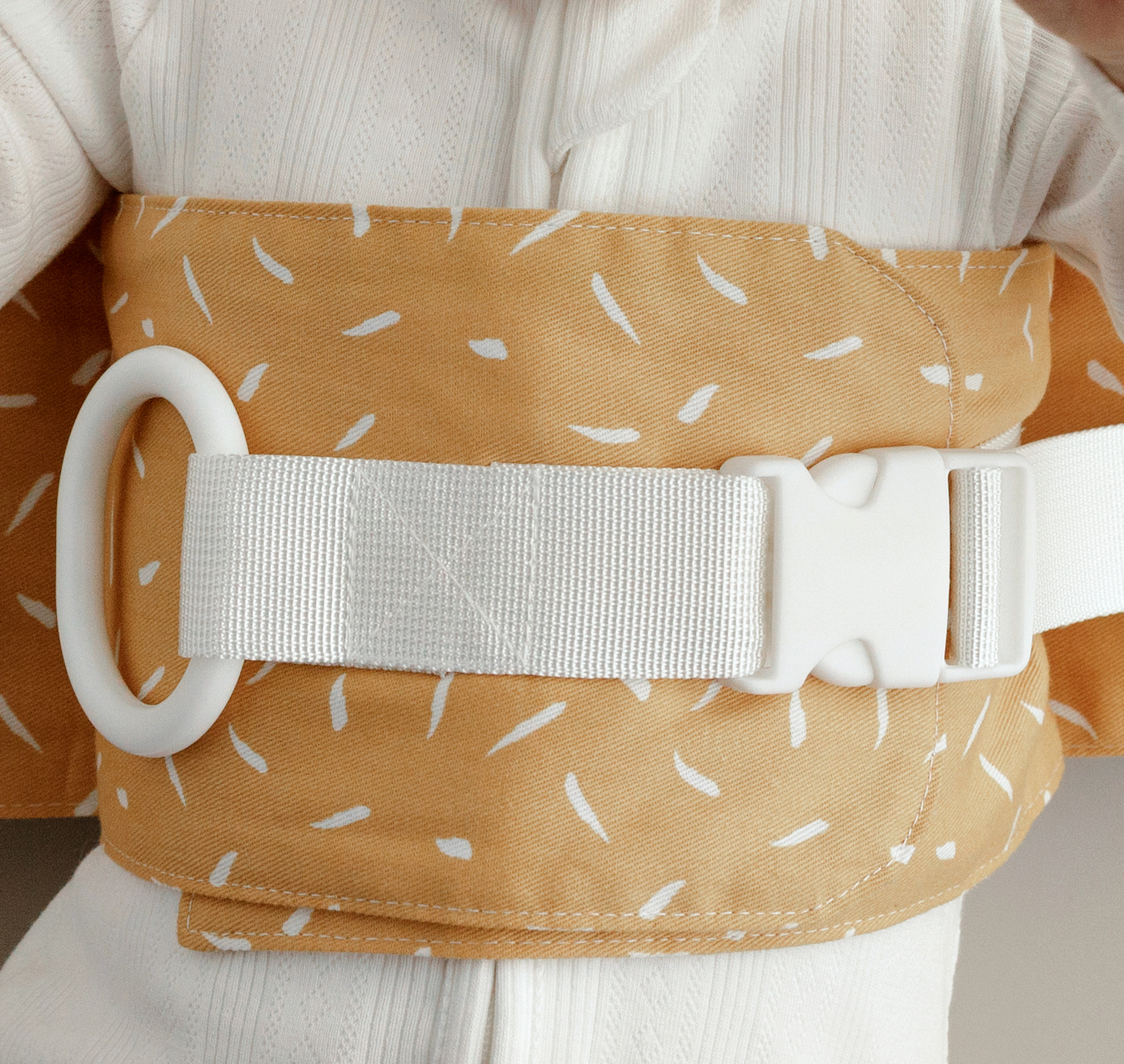 Close up of mustard yellow WriggleBum nappy change harness, with white straps and buckle.