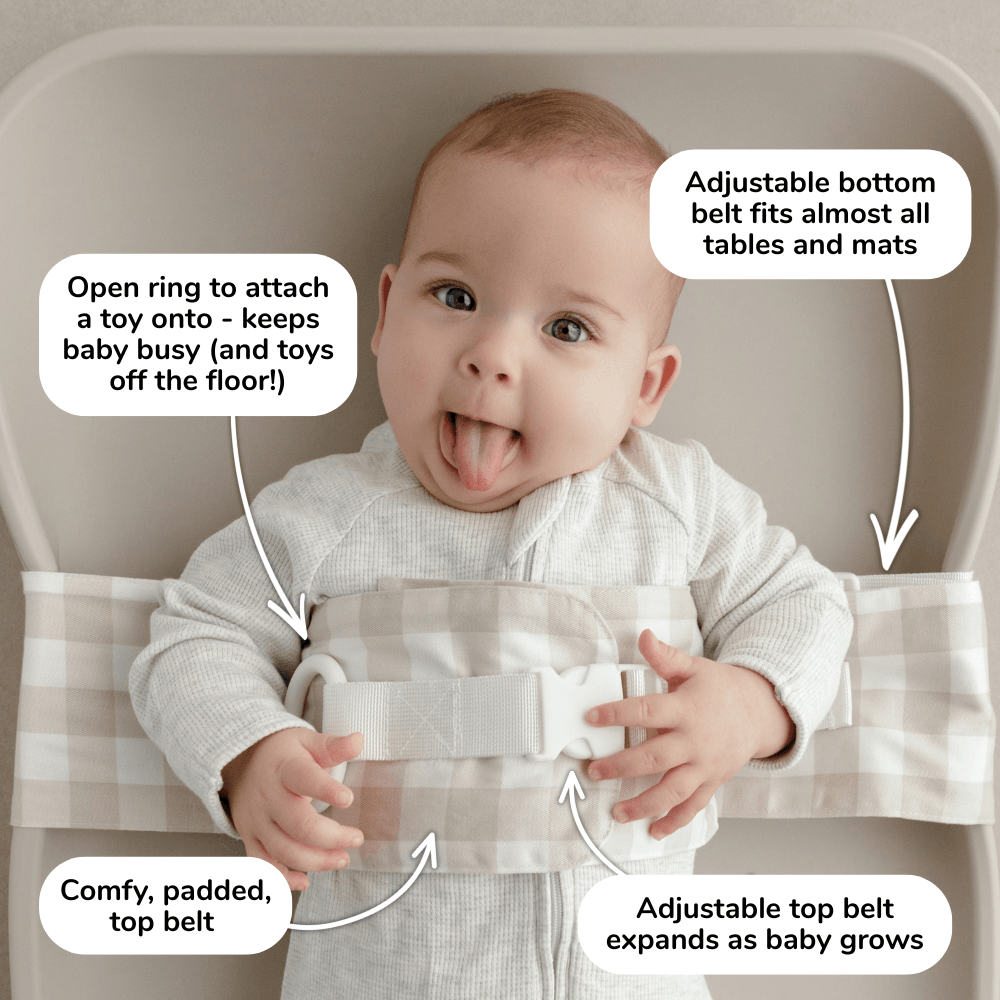 Baby lies on a change mat with an Oatmeal Afternoon WriggleBum nappy change harness wrapped around them. 
Four white bubbles highlight the key features of the harness: 
- Open ring to attach a toy onto - keeps baby busy (and toys off the floor!)
- Adjustable bottom belt fits almost all tables and mats 
- Adjustable top belt expands as baby grows
- Comfy, padded top belt