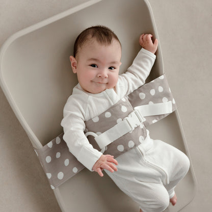 Smiling baby lying on a change mat, with a Spotty Dotty WriggleBum nappy change harness wrapped around them. 